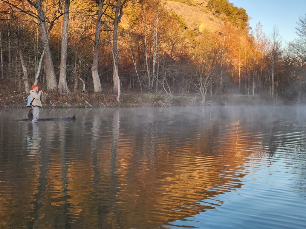 Riverscape image of man fishing andwading in the river